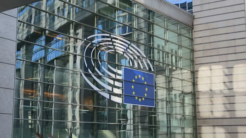 Szklana fasada budynku Parlamentu Europejskiego w świetle dziennym z emblematem Unii Europejskiej.