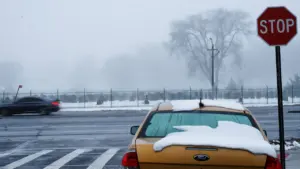 Samochód przykryty śniegiem na parkingu przy cmentarzu przed świętem Wszystkich Świętych.