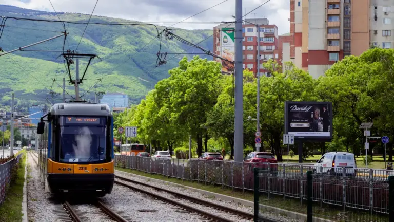 Nowoczesny tramwaj poruszający się po torach w otoczeniu miejskiej zieleni i budynków.