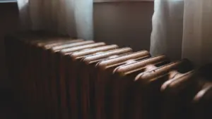 Standardowy biały grzejnik zamontowany na ścianie w typowym mieszkaniu przygotowanym do sezonu grzewczego.