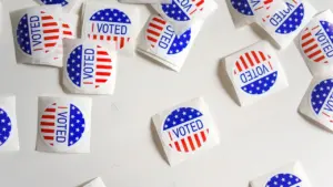 Wiele okrągłych naklejek z napisem I VOTED na tle amerykańskiej flagi na białym tle.