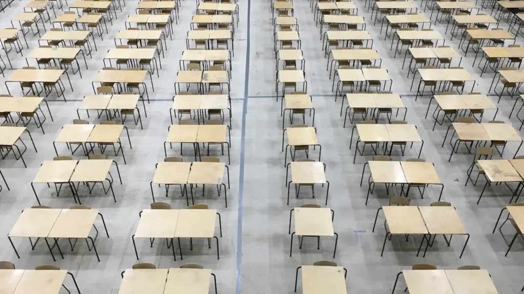 Pusta sala egzaminacyjna z rzędami drewnianych stolików i krzeseł widziana z góry