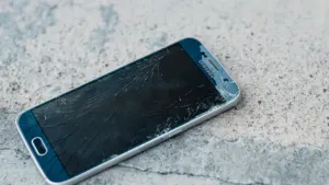 Rozbity smartfon leżący na szarej nawierzchni, symbolizujący zagubienie, stres i utratę kontroli.