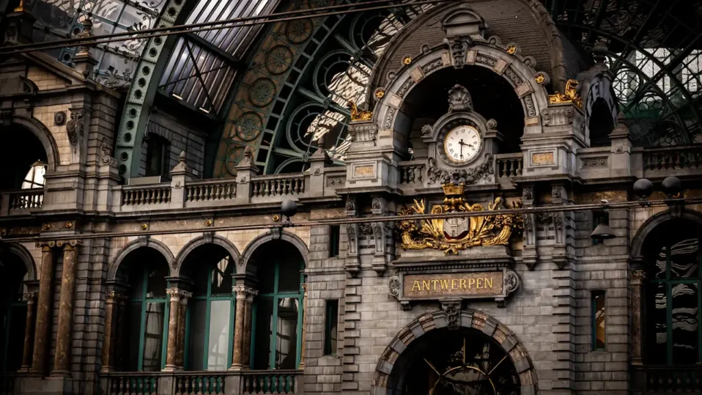 Historyczny zegar na dworcu kolejowym w Antwerpii, przypominający o zmianie czasu w podróży.