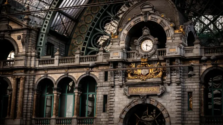 Historyczny zegar na dworcu kolejowym w Antwerpii, przypominający o zmianie czasu w podróży.